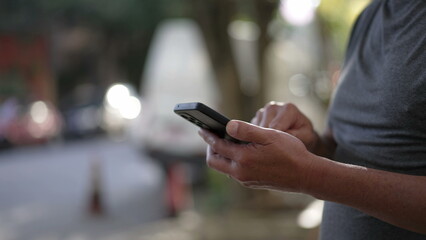Person using cellphone standing outdoors in city street sidewalk. Closeup hands holding smartphone device texting message