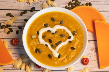Pumpkin soup with cream and pumpkin seeds isolated on wooden background, top view. Autumn concept. 