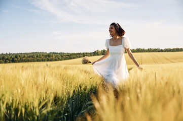 Having a walk. Beautiful young bride in white dress is on the agricultural field at sunny day