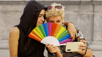 a non-binary persons with a rainbow hand fan looking at mobile. Gay Pride's day