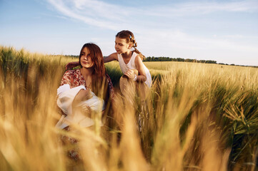 Woman is sitting on the ground. Mother with her newborn baby and girl is on the field at sunny day together