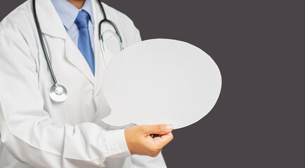 Doctor in uniform holding a blank speech bubble while standing on a gray background