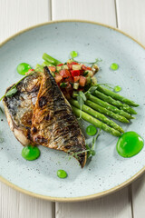 Halved grilled sea bass fish with fresh asparagus and vegetables on plate