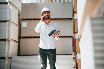 Having conversation by phone. Storage worker is in the warehouse with bunch of products