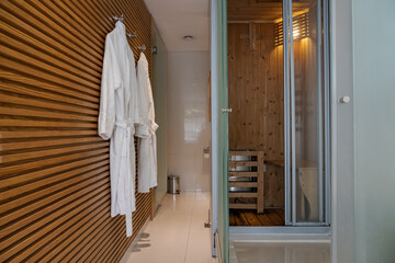 Sauna inside a hotel room with clean white bathrobes hanging on the wall