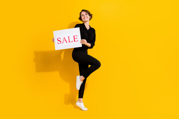 Fototapeta na wymiar Full size photo of sweet young short hair lady hold poster sale wear shirt jeans shoes isolated on yellow color background