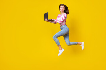 Fototapeta na wymiar Full size photo of pretty young lady running hold laptop digital nomad dressed trendy striped clothes isolated on yellow color background