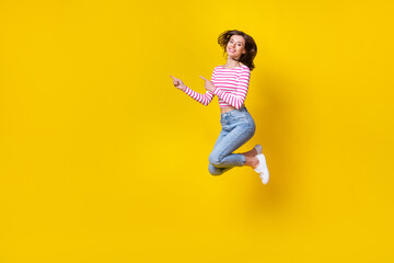Fototapeta na wymiar Full length photo of positive cheerful girl wear striped top jeans sneakers directing empty space isolated on yellow color background
