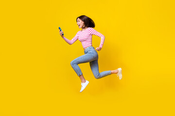 Fototapeta na wymiar Full size photo of pretty young girl running hold device fast connection wear stylish striped garment isolated on yellow color background