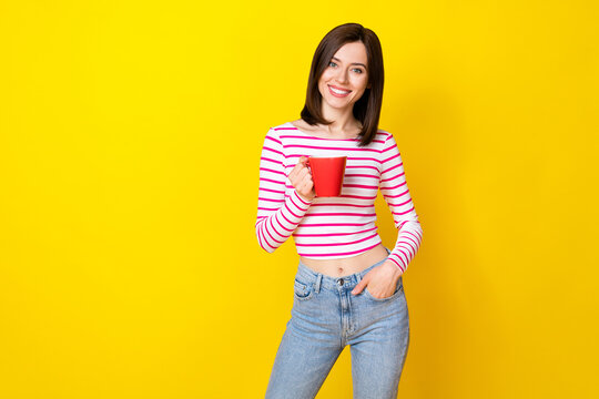 Photo portrait of nice young girl hold red tea mug chatting colleagues dressed trendy striped outfit isolated on yellow color background