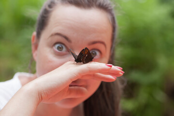 Portrait of an adult happy brunette woman holding butterflies in her hand in a forest clearing and showing psychological appeasement