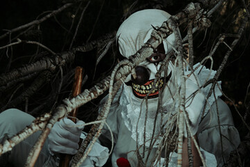 evil clown with an axe in the woods at night
