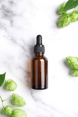 Aromatic or essential oil in bottle with fresh hop cones on a marble background