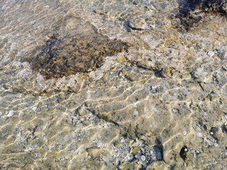The coast of the Mediterranean Sea, clear water with reflections of the sun's rays, through which you can see the stone bottom. Background.