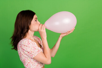 Side profile photo of young adorable pretty cute nice lady wear pink summer top blow inflate big air balloon funny face crazy isolated on green color background