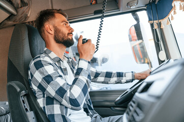 Using radio. Young truck driver is with his vehicle at daytime