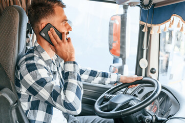 Talking by phone. Young truck driver is with his vehicle at daytime © standret