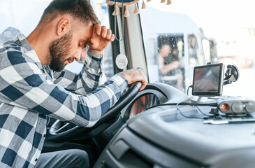 Tired of work. Sitting in the cabin. Young truck driver is with his vehicle at daytime
