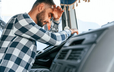 Tired of work. Sitting in the cabin. Young truck driver is with his vehicle at daytime