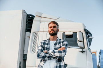 With arms crossed. Young truck driver is with his vehicle at daytime