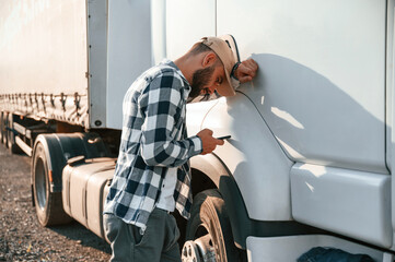 Feeeling tired. Using smartphone. Young truck driver is with his vehicle at daytime