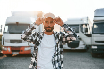 Front view. In cap. Young truck driver is with his vehicle at daytime © standret
