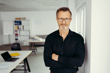 Portrait of smiling senior man standing in office corridor wearing glasses