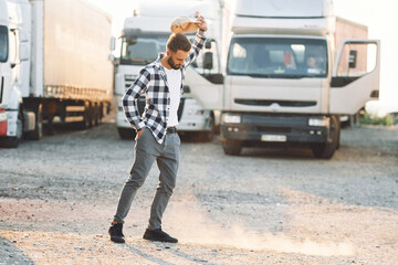 Standing and feeling bored. Young truck driver is with his vehicle at daytime