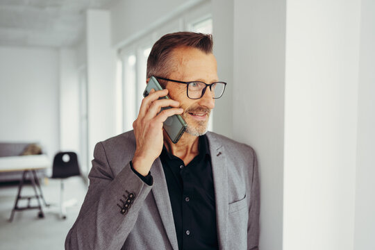 Smiling mature businessman with glasses talking on cell phone