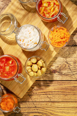 Probiotic food. Pickled or fermented vegetables. Lecho, sauerkraut, ajvar, korean carrot, olives in glass jars on a wooden background with shadows. Home food preserving or canning. Flat lay