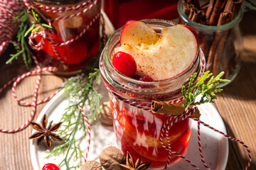 Hot mulled wine with cinnamon and star anise. Winter autumn fruit and berry grog, hot punch drink with orange, apple, cranberry, spices, with Christmas tree branches and gift boxes on wooden table 