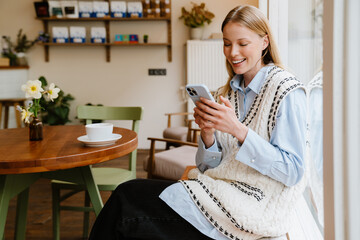 Young beautiful smiling woman with phone sitting in cafe