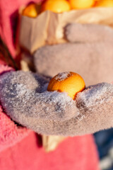 Woman in a pink coat holds a craft bag with tangerines in her hands, walking in a snowy winter park.Hands in mittens close-up.Festive mood.New Year,Christmas, winter concept.