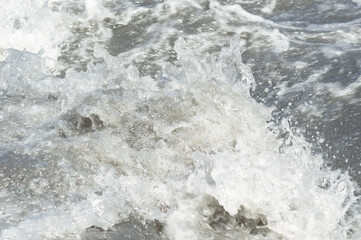 Close-up white water of the mountain stream in a summer day. White and grey foam of waves and drops...