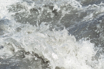 Close-up white water of the mountain stream in a summer day. White and grey foam of waves and drops of water