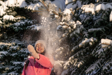 Fototapeta na wymiar Young beautiful happy woman in pink coat stands under the snow falling from spruce branches in a winter forest.Winter concept.Selective focus.