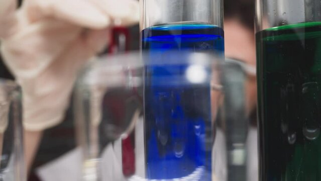 Row of test tubes with colorful liquids and doctor checking red blood sample in laboratory slow motion. Probe lens footage of experiment closeup