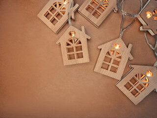 Golden light garland with wooden small houses on brown background with copy space. Christmas post...