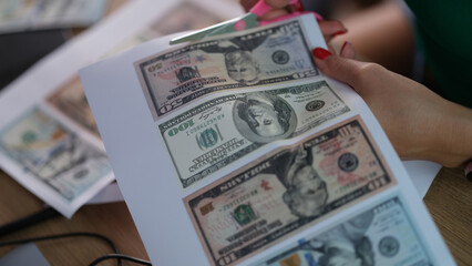 Counterfeiter cuts dollar bills with scissors closeup