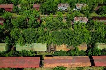 Top view above an industrial railroad yard with derelict freight cars stationed on unused railroad tracks covered by overgrown lineside vegetation