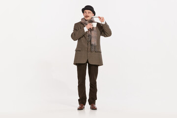 Portrait of stylish man in suit, coat and cap posing with tea cup over white background. English man