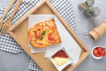 Pizza bread topped with shrimp, crab sticks, tomatoes, cheese in a wooden tray