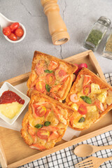 Pizza bread topped with shrimp, crab sticks, tomatoes, sausage, cheese in a wooden tray