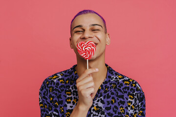 Young handsome stylish short-haired happy boy covering mouth with lollipop