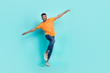 Fototapeta na wymiar Full length photo of excited funky man dressed orange t-shirt smiling dancing arms sides isolated turquoise color background
