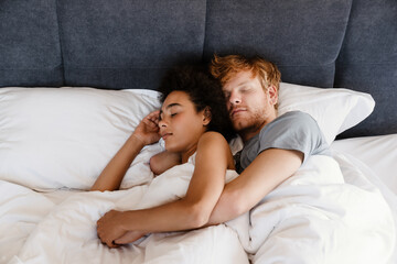 Young multinational couple hugging and sleeping together at home