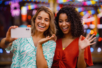 Young multiracial women taking selfie on cellphone in attraction park