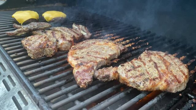 two cheeseburgers beef patties and staks on a firry gas grill on a summer sunny holiday