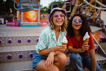 Young multiracial women eating ice cream in attraction park