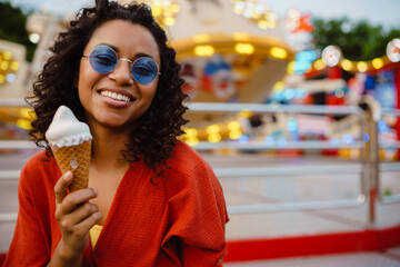 Young black woman eating ice cream in attraction park